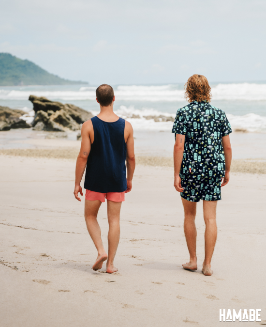 Two men on a beach wearing beachwear from Hamabe:  a cotton tank top and a short sleeve shirt - Bikini Village 